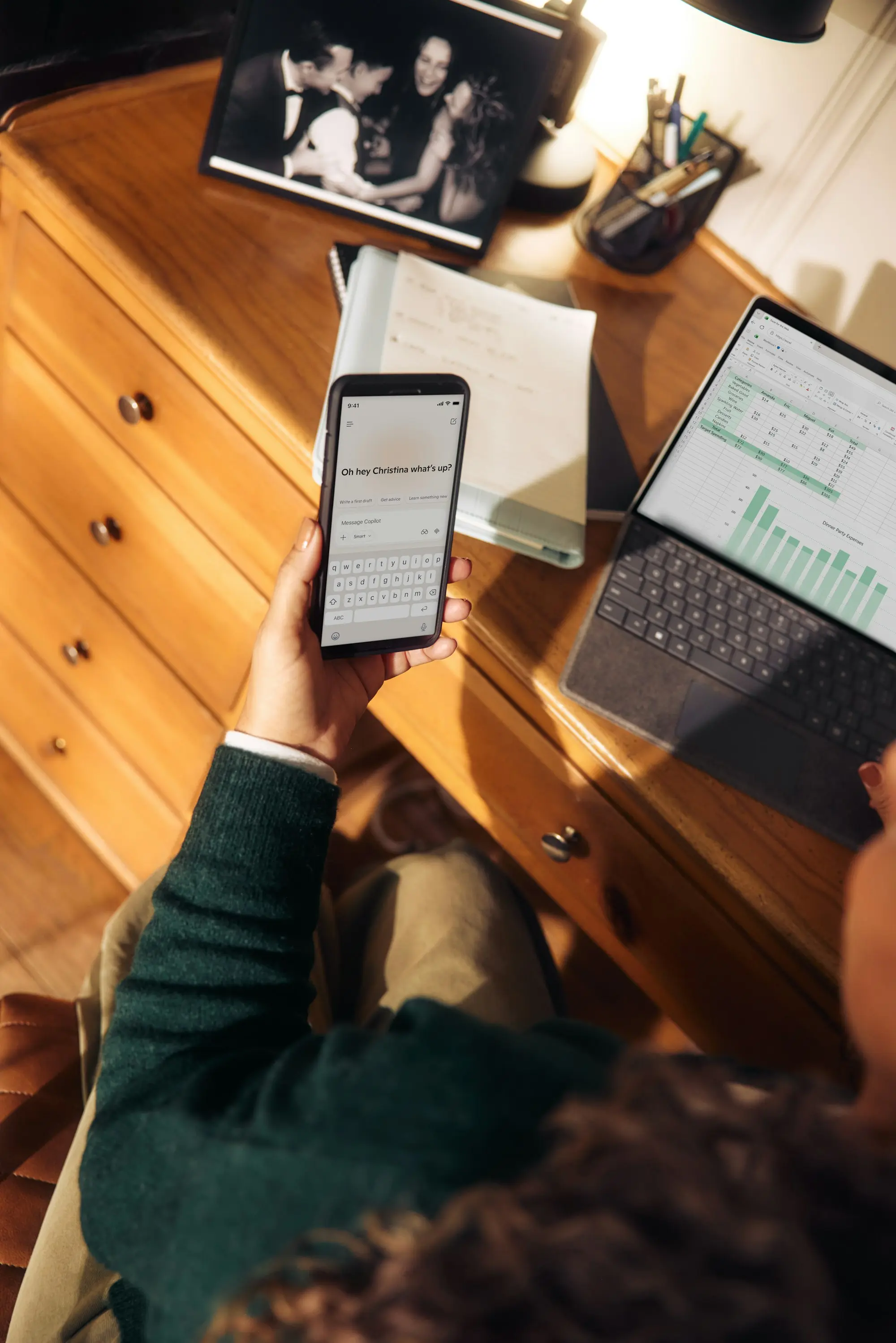 Une main tient un téléphone au-dessus d'un bureau où un ordinateur affiche des graphiques